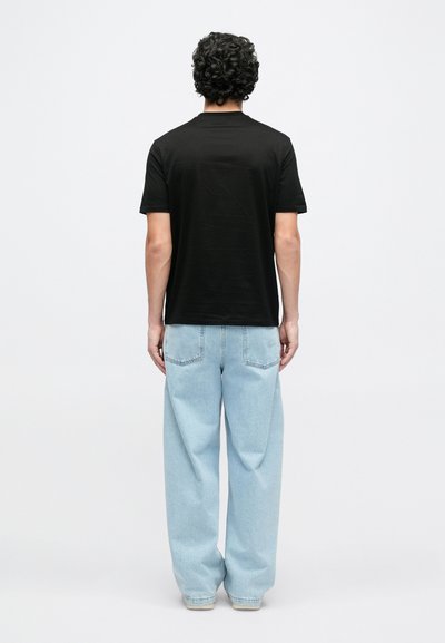 Μαύρο κοντομάνικο T-shirt με στρογγυλή λαιμόκοψη, συνδυασμένο με ανοιχτό μπλε, φαρδιά τζιν παντελόνια. Απλός σχεδιασμός, χωρίς έντονα μοτίβα.