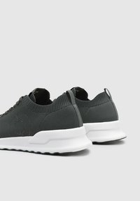Zapatillas de malla grises con un cuello acanalado, suela blanca y un diseño minimalista. Presentan una lengüeta y paneles laterales texturizados.