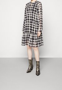 Robe à manches longues en noir et blanc à carreaux avec un ourlet à volants et une fermeture à nouer, associée à des bottines métalliques en imprimé serpent.