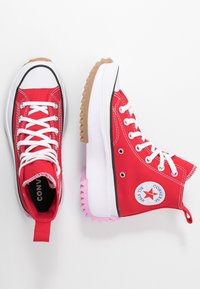 Baskets montantes en toile rouge avec lacets blancs et semelle en caoutchouc. Présentent une bordure noire, un logo étoile et une semelle accentuée de rose.