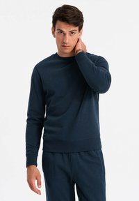 Sudadera azul marino en una suave tela texturizada. Cuello y puños de canalé, con una sutil etiqueta de logo en el dobladillo. Corte ajustado.