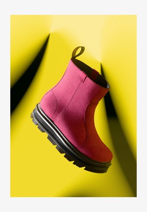 Magenta gležnjače s teksturiranom površinom, trakom za povlačenje i debelim crnim potplatom s robustnim uzorkom za hodanje. Postavljene na žutoj pozadini.