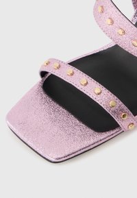 Pink metallic heeled sandal with a square toe, featuring three straps embellished with gold studs, and a black textured insole.