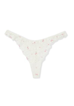 String en dentelle blanche avec petits motifs floraux roses et bords festonnés, posé à plat sur un fond blanc.
