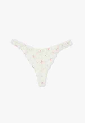 String en dentelle blanche avec petits motifs floraux roses et bords festonnés, posé à plat sur un fond blanc.