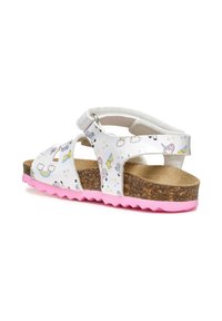 Sandalias blancas con un patrón repetido de unicornios y nubes, suela de goma rosa, plantilla de corcho, correa ajustable y diseño troquelado.