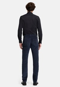 Pantaloni in corduroy blu scuro con vestibilità dritta, dotati di due tasche posteriori e un tessuto testurizzato. Abbinati a una camicia nera a maniche lunghe.