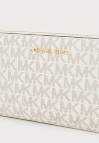 Michael Kors denarnica v bež platnu z ponavljajočim se vzorcem MK, ki ima zlat logo, zadrgo in gladko teksturo.