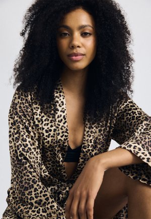Leopard print robe in soft fabric, featuring a deep V-neck, wide sleeves, and a relaxed fit, worn over a black top. Natural curly hair.