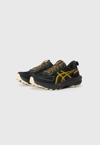 Chaussures de sport noires et jaunes avec une tige en maille, semelle beige, motifs texturés et design durable. Comprend des lacets et des accents de marque.