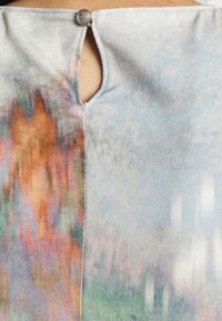 Haut multicolore sans manches en tissu doux et lisse, avec une ouverture goutte d'eau dans le dos, maintenue par un bouton métallique.