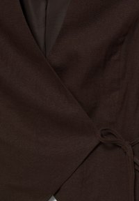Gros plan d'un tissu marron foncé avec un nœud noué sur le côté droit, montrant la texture et les couches superposées.