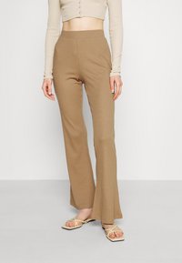 Bruna, randiga, vida byxor med hög midja. Bärs med en ljus långärmad topp och beiga sandaler med remmar.