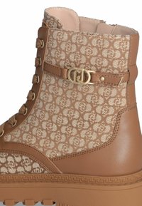 Bottine marron avec un motif texturé, ornée d'un accent en doré, conçue avec des lacets, et dotée d'une semelle en caoutchouc robuste.