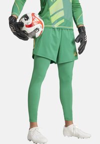 Completo del portiere verde composto da maglia a maniche lunghe con design grafico, pantaloni coordinati, leggings verdi, guanti neri e scarpini bianchi.