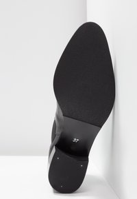 Semelle de chaussure noire tournée vers le haut avec le numéro de taille 37 imprimé près du talon, montrant des zones de grip lisses et texturées.