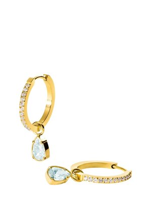 Goldene Creolen mit kleinen klaren Steinen auf dem Ring und einem hängenden birnenförmigen klaren Edelstein an jedem Ohrring, gezeigt auf weißem Hintergrund.