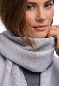 Szary dziergany szalik o miękkiej fakturze, z grubym kołnierzem kominowym, ściśle owinięty wokół szyi, podkreślający jego ciepło i wygodę.