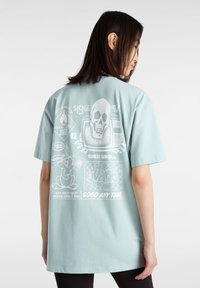 Camiseta de algodón verde menta con estampados gráficos en la parte posterior, incluyendo una calavera, un televisor vintage y un personaje de dibujos animados. Mangas cortas, corte relajado.