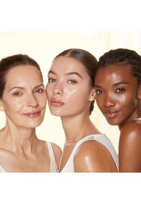 Drei Frauen mit verschiedenen Hauttönen, die weiße Oberteile tragen. Sie haben glatte, strahlende Haut, vor einem hellen Hintergrund, der ihre Merkmale hervorhebt.