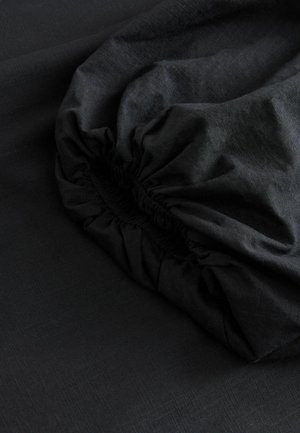 Tessuto nero con una superficie liscia, dotato di una cintura elastica arricciata. Il materiale presenta una leggera lucentezza e un leggero motivo.