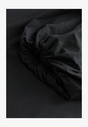 Tessuto nero con una superficie liscia, dotato di una cintura elastica arricciata. Il materiale presenta una leggera lucentezza e un leggero motivo.