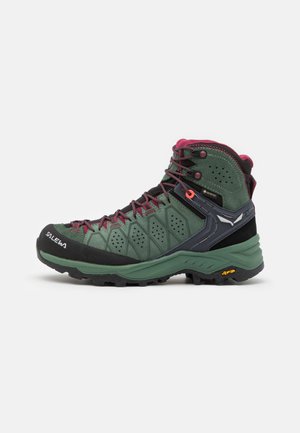 Green hiking boot with a textured surface, purple accents, black rubber toe cap, and Vibram sole, featuring reinforced eyelets and breathability holes.