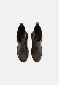Bottines en cuir marron avec un bout arrondi, doublure en tissu côtelé et fermeture éclair sur le côté. Présente une semelle en caoutchouc noir basse.
