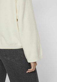 Pull en maille ivoire à coupe décontractée, avec un ourlet et des poignets côtelés, assorti à un jean gris foncé avec un design de poche minimaliste.