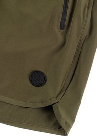 Oliwkowa kurtka o gładkiej fakturze, z czarną kieszenią na zamek błyskawiczny i okrągłą czarną łatką z logo w dolnej części.