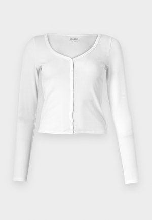 Weißes Langarmshirt aus geripptem Stoff, mit einem Rundhalsausschnitt und durchgehender Knopfleiste. Figurbetonte Passform mit subtiler Textur.