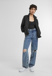 Svart zip-up jakke over en svart tank topp, kombinert med lyseblå ripped jeans og hvite sneakers, med avslappet passform og uformell stil.
