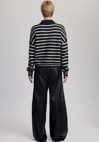 Mustavalkoraidallinen neulepaita, jossa on pyöreä pääntie ja löysä istuvuus, yhdistettynä laaja lahkeisiin mustiin nahkahousuihin. Pehmeä pinta, rento siluetti.