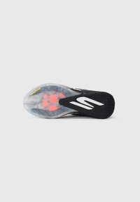 Semelle de chaussure de sport noire avec un fond translucide en caoutchouc présentant des coussins de rembourrage rose et un logo blanc proéminent. Marque Goodyear présente.