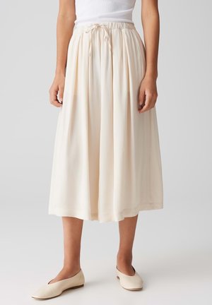 Mujer con falda midi color crema con cinturilla elástica y cordón, combinada con bailarinas crema a juego.