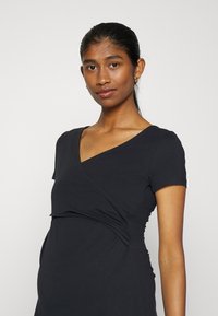 Vestido de maternidade preto com um design de decote em V, mangas curtas e detalhes franzidos nas laterais, feito de um tecido macio e elástico.