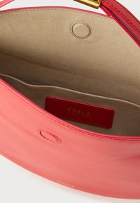 Ροζ δερμάτινη τσάντα χειρός με λεία εξωτερική επιφάνεια και απαλό, μπεζ εσωτερικό. Διαθέτει χρυσή ετικέτα μάρκας και στρογγυλό κλείσιμο με κουμπί πίεσης.