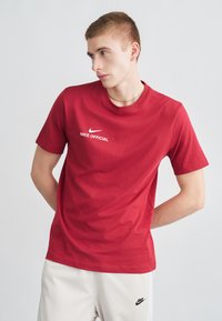 Červené tričko Nike z bavlny s okrúhlym výstrihom a krátkymi rukávmi, so bielym logom "NIKE OFFICIAL" na hrudi. Hladká textúra.