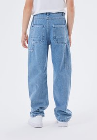 Ljust blå denimjeans med avslappnad passform, med två bakfickor och rak ben-design, bärs tillsammans med vita sneakers.