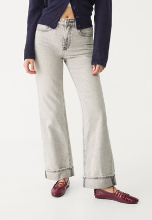 Jeans wide en denim gris clair avec une taille haute, présentant des coutures visibles et des ourlets retroussés. Associés à des ballerines bordeaux.