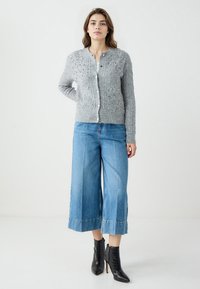 Grijze gebreide cardigan met een textuurpatroon en parelaccenten, gecombineerd met wijde denim broek en zwarte enkellaarzen.