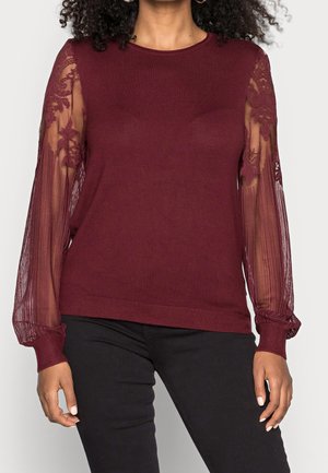 Pullover bordeaux con maniche lunghe a strisce trasparenti e dettagli in pizzo floreale. Le maniche a costine e l'orlo creano un contrasto di texture.