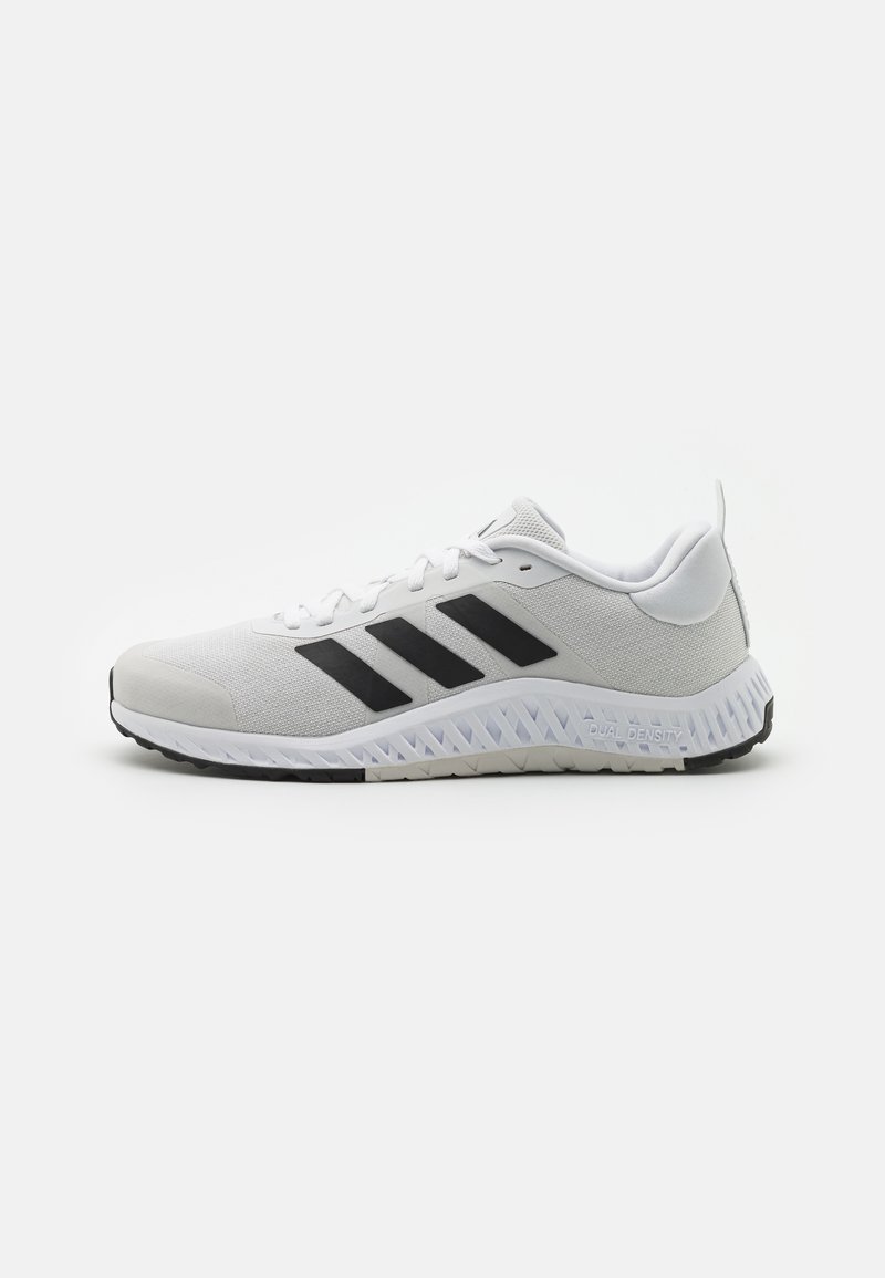 White athletic shoe with black stripes, mesh upper, rubber sole, and textured accents. Features a rounded toe and padded collar.