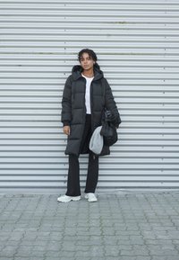 Svart pufferjacka med huva, vit t-shirt, svarta byxor och vita sneakers. Tillbehör inkluderar en grå scarf och en svart väska.