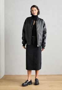 Giacca bomber nera in pelle liscia, abbinata a un dolcevita nero aderente e a una gonna nera al ginocchio. Scarpe slip-on nere chunky.