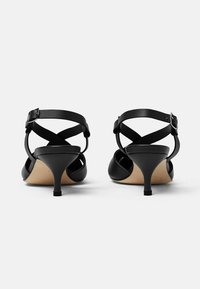 Crne sandale na visokom potplatu s uskim vrhom, dizajnom s križnim trakama, podesivom kopčom oko gležnja i tankom, stiletto potpeticom. Glatka kožna tekstura.