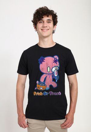 Ung mand smilende iført sort t-shirt med lyserbjørn, der holder slik og en græskarbøtte med teksten "Trick Or Treat".