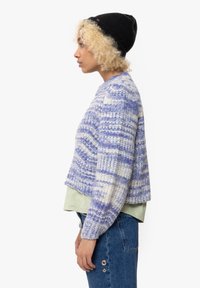 Strikket cropped sweater i lyse lilla og hvide striber. Blød tekstur med rund halsudskæring, båret over en lys grøn top og blå jeans.