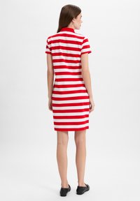 Rood-wit gestreepte polo jurk met een kraag, korte mouwen, een aansluitende pasvorm en een rechte zoom, gecombineerd met zwarte platte schoenen.