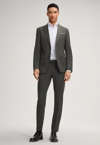 Completo grigio scuro con un design aderente, giacca monopetto, revers a punta e una camicia bianca a righe sottili. Scarpe eleganti nere completano l'outfit.